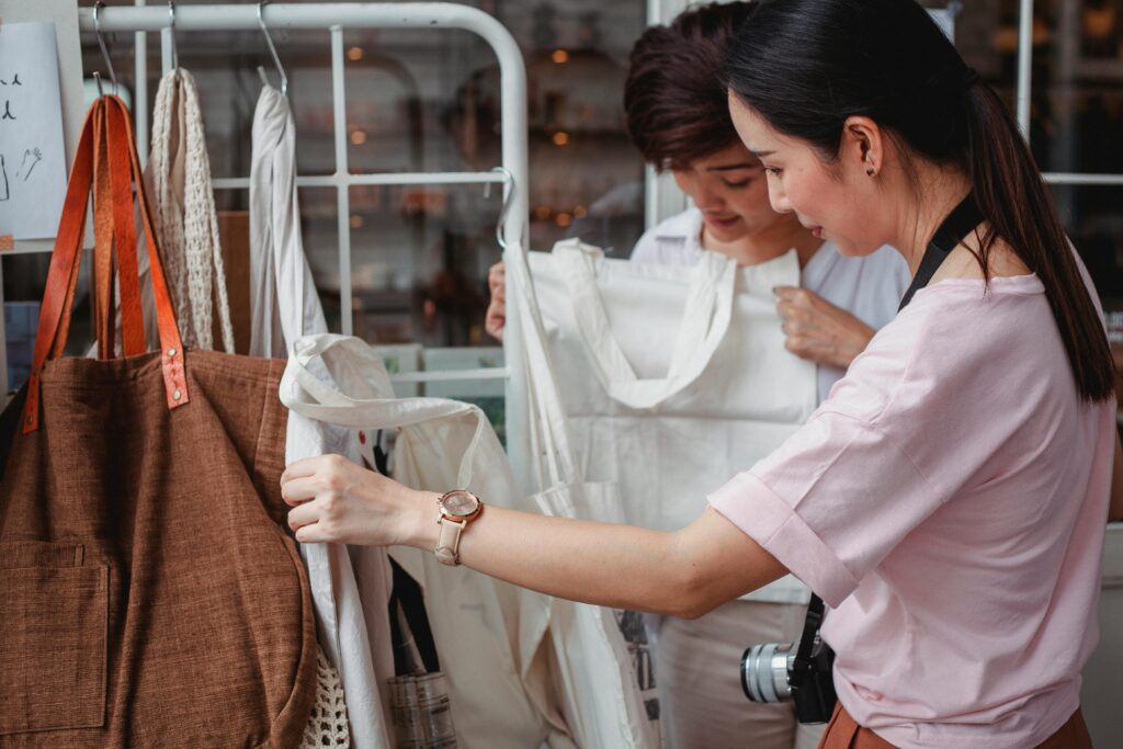 Two women examining eco-friendly bags in a fashionable boutique setting, highlighting sustainable shopping.