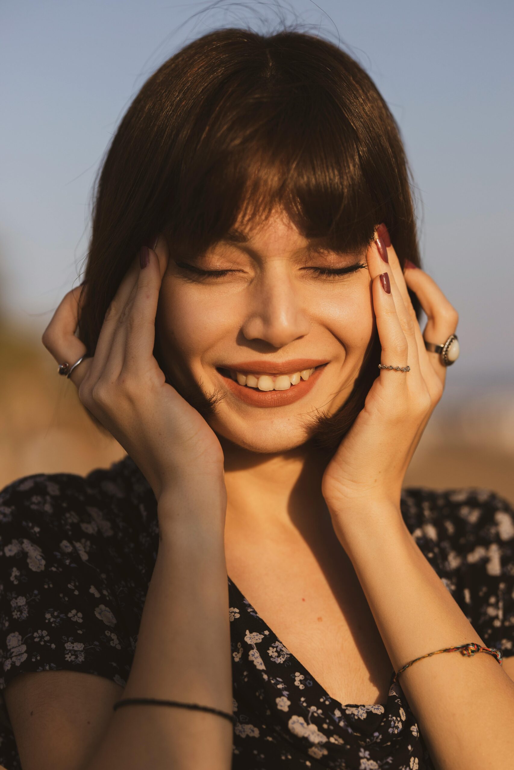 A smiling young woman enjoying a sunny day outdoors with her eyes closed.